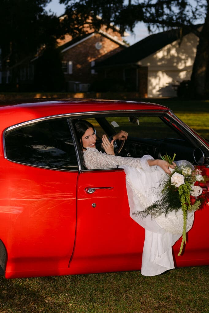 Florida bride sitting in a vintage red getaway car during her wedding day